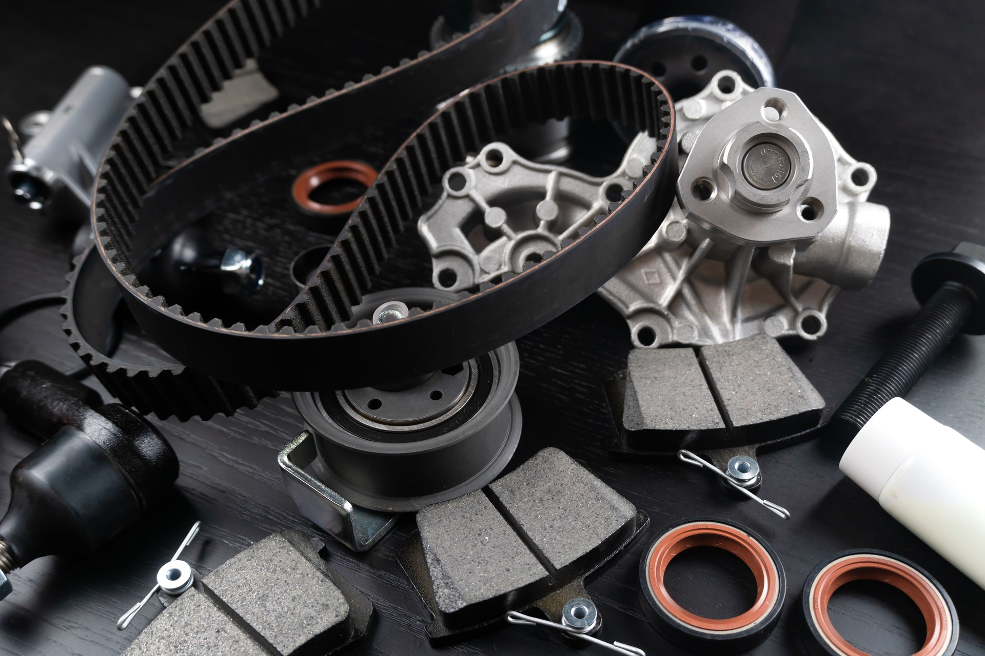 Lot of auto parts lie on wooden black background. Engine and suspension parts, swivel knuckle, joint and engine parts unfolded. New spare parts. Bearings . Play by light. Hanging on table.